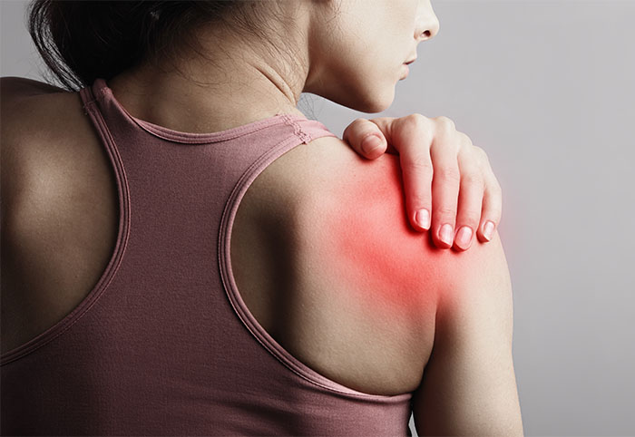 Young strong sporty woman suffering from pain in shoulder in sport wear. Touching the hand. Sports exercising injury. Closeup portrait with highlighted in red and empty copy space. Back view. The concept of medicine, massage, physiotherapy.